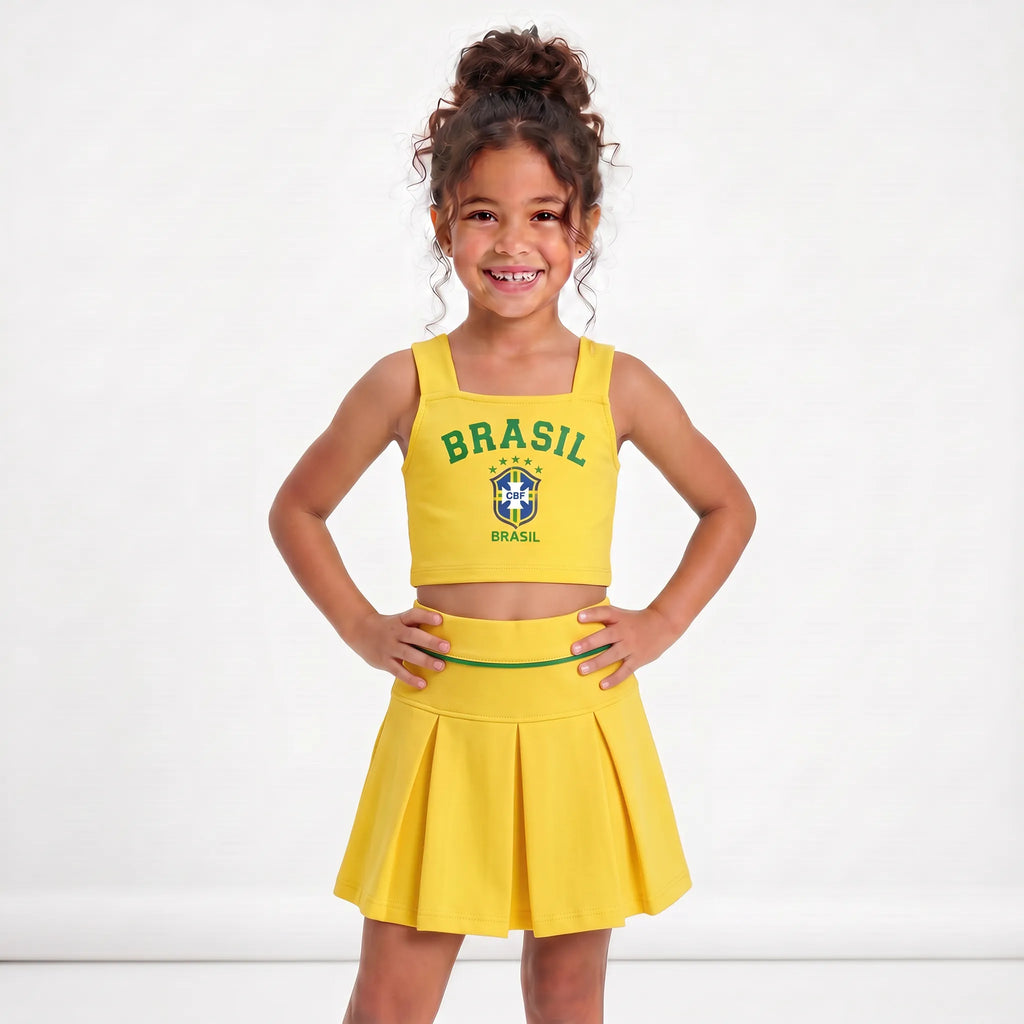 Menina vestindo conjunto infantil saia plissada cropped brasil brasão amarela — look Copa 2026 VAI DAR BRASIL charme elegante