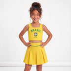 Menina vestindo conjunto infantil saia plissada cropped brasil brasão amarela — look Copa 2026 VAI DAR BRASIL charme elegante
