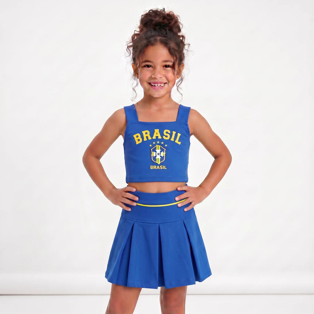 Menina vestindo conjunto infantil saia plissada cropped brasil brasão azul — look Copa 2026 VAI DAR BRASIL charme elegante